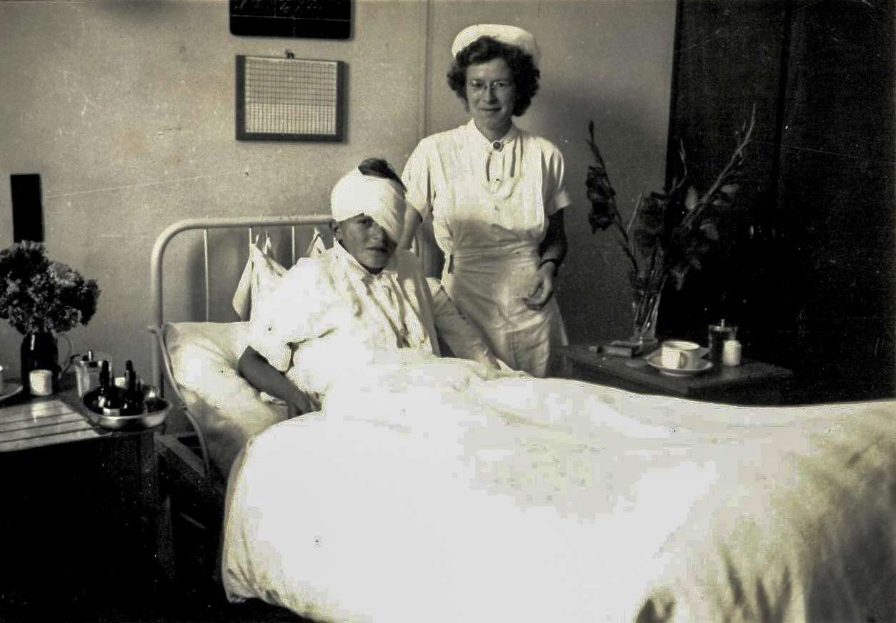 Sygeplejerske med en sengeliggende dreng med stor øjenforbinding. Thisted Sygehus 1946.jpg