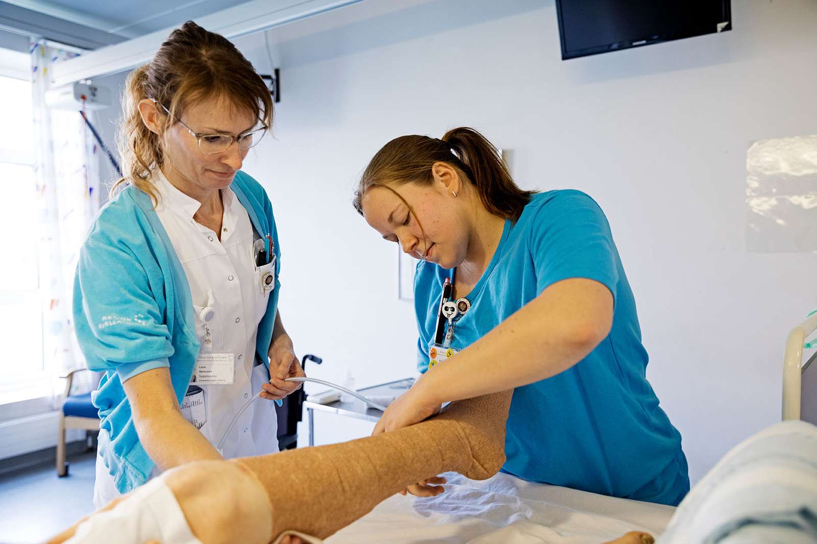 To sygeplejersker tjekker en patients ben 