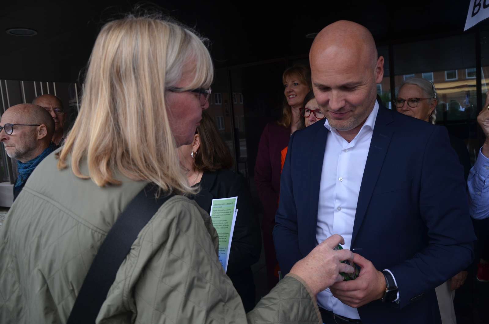 Marianne Østerlund Madsen, FTR på AUH, overrækker Regionsrådsformand Anders Kühnau en energidrik med en opfordring om at råbe Christiansborg op for flere penge til sundhedsvæsenet.