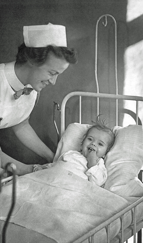 Sygeplejerske stå bøjet over et 1-2 årigt barn, liggende i en hospitalsseng