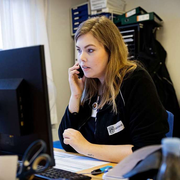 En sygeplejerske taler i telefon ved et skrivebord.