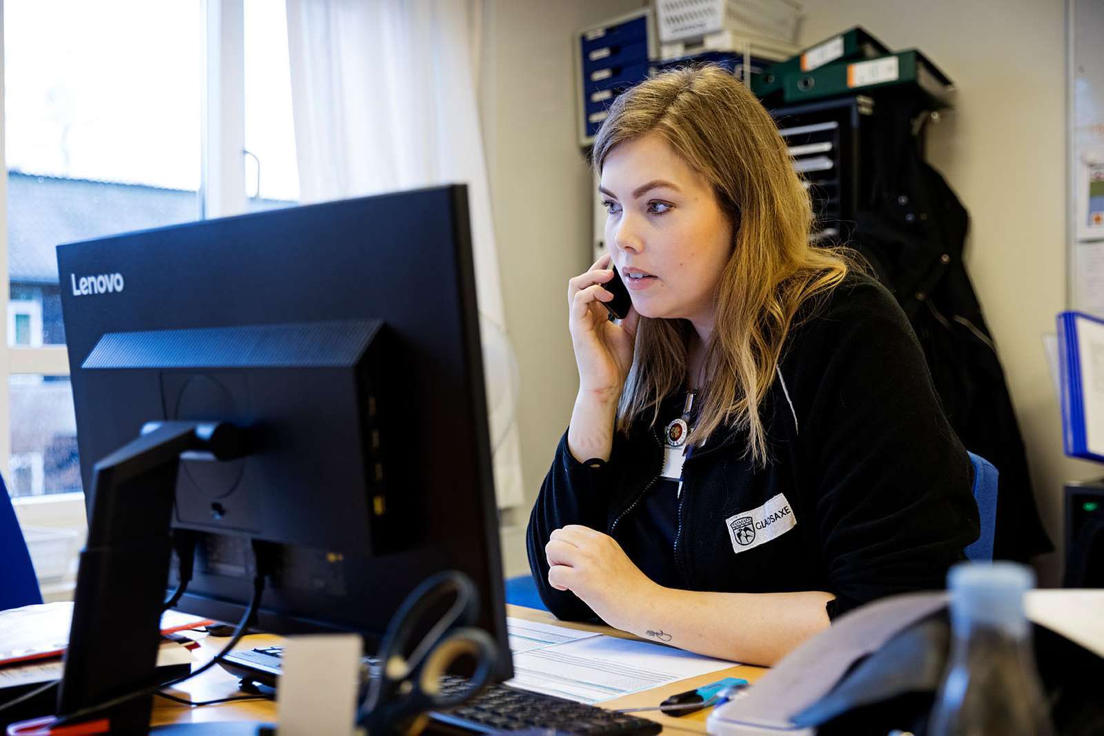 En sygeplejerske taler i telefon ved et skrivebord.