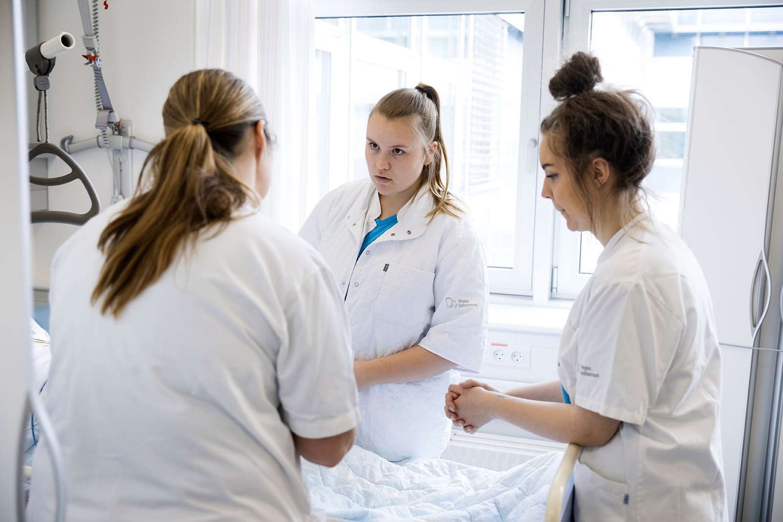 Tre sygeplejersker ved en patient.