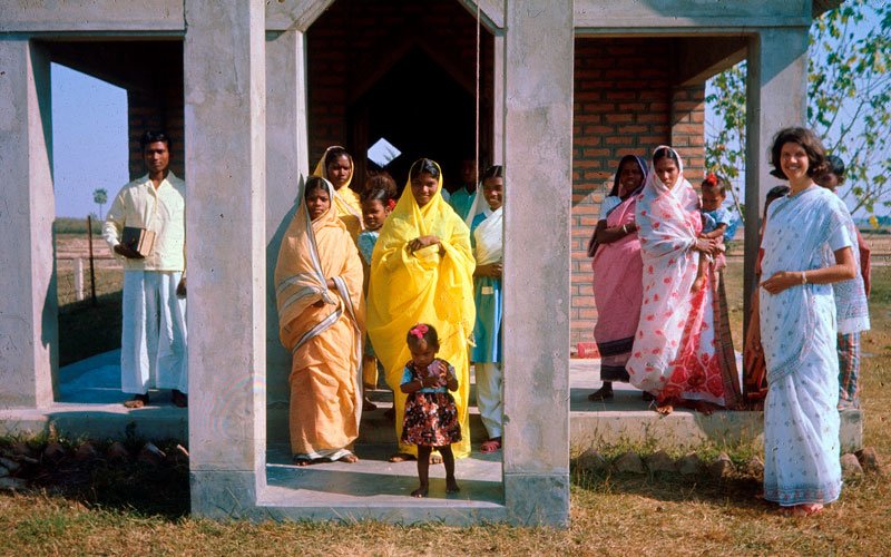 1971. En flok af Amnuras borgere efter
            gudstjeneste i byens kirke. Ruth Frost Egedal bærer en hvid udgave af den Sydasiatiske dragt ’sari’.