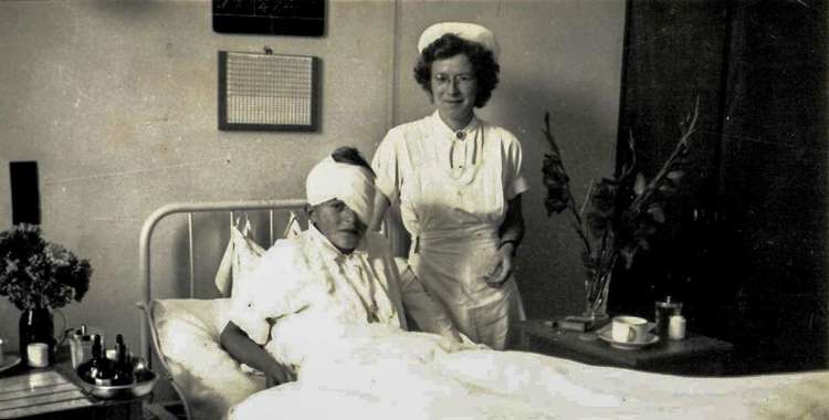 Sygeplejerske med en sengeliggende dreng med stor øjenforbinding. Thisted Sygehus 1946.jpg